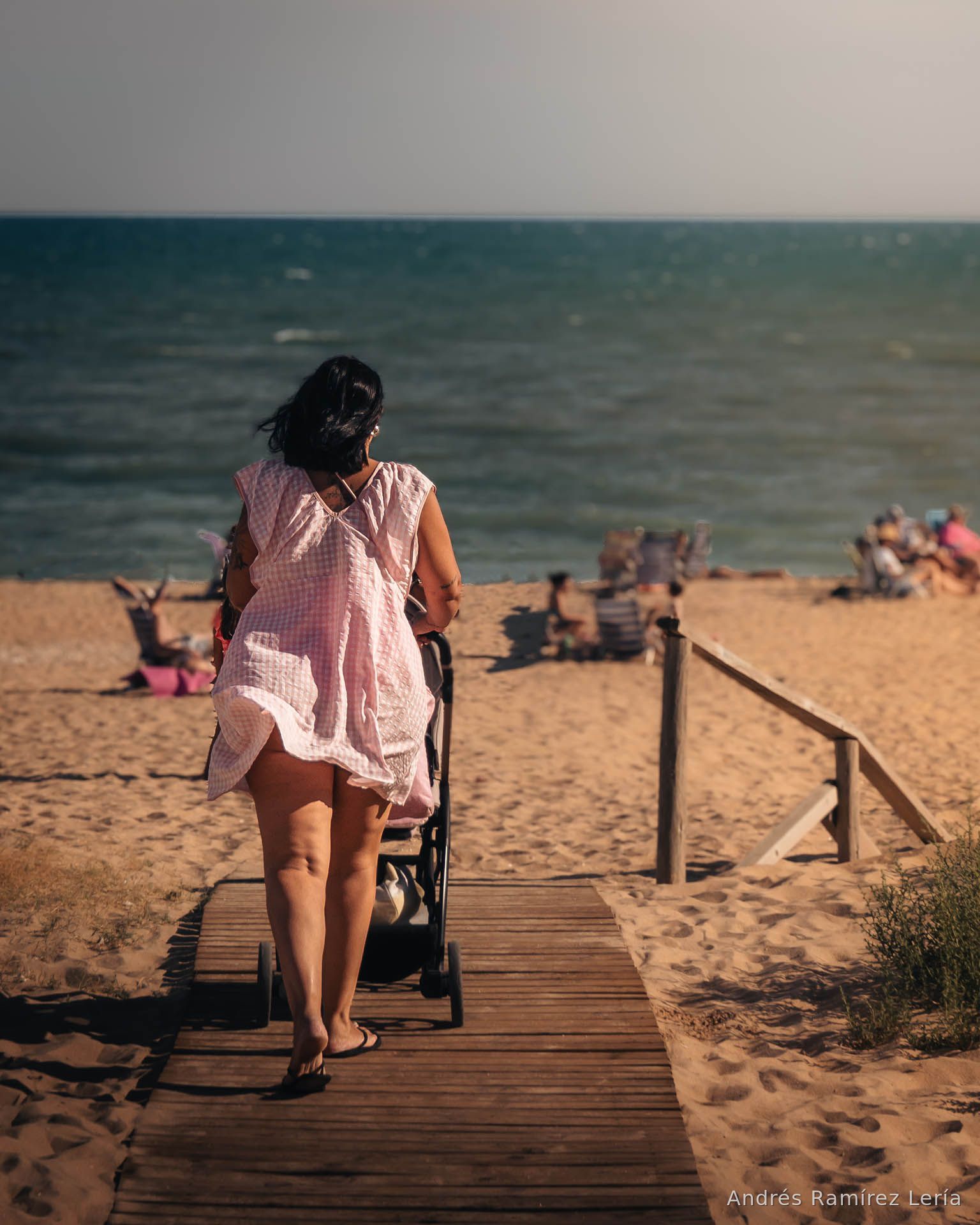 Hay algo muy de #LaAntilla en esta imagen: bajar por la pasarela, sentir la arena cerca, ver el mar abrirse delante y encontrar la playa todavía viva al caer la tarde. Julio deja aquí una escena cotidiana pero llena de verano, con pasos lentos, cuerpos relajados, viento de poniente y esa sensación de que el día se alarga un poco más junto al mar.